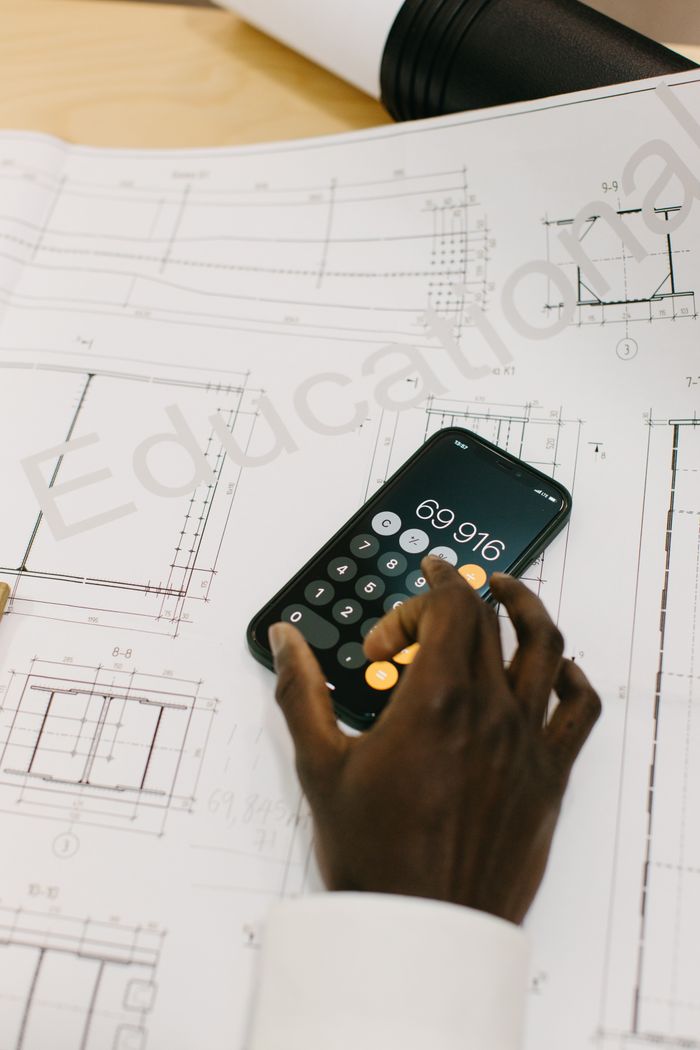 About Hand using smartphone calculator on architectural blueprints. Modern technology in engineering.