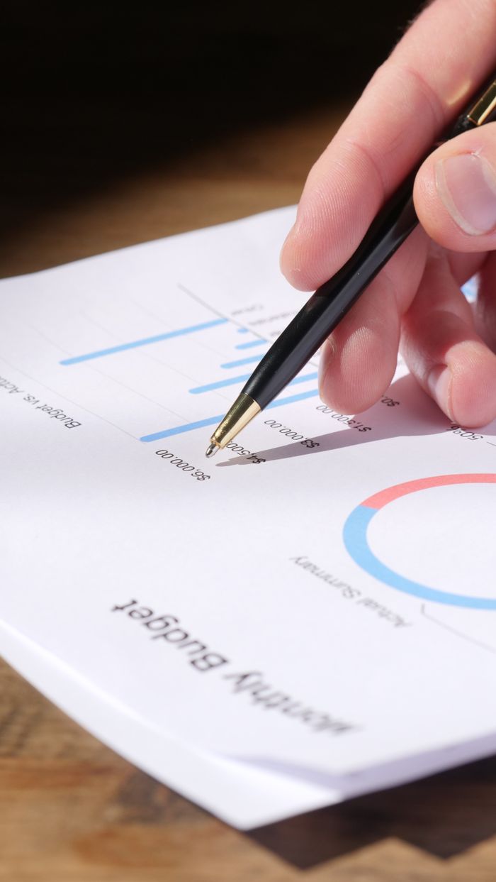 Home Close-up of hand analyzing data on a monthly budget document with graphs and charts.